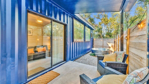 A modern house with large sliding glass doors, a patio with wicker furniture, and a wooden deck.