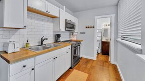 A compact kitchen with white cabinets, a microwave, a stove, and a sink.