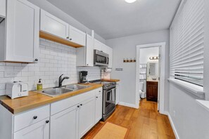 A compact kitchen with white cabinets, a microwave, a stove, and a sink.