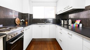 A modern kitchen with white cabinets, a black countertop, a stainless steel stove, and a window above the sink. - Coastal 2-bed With Balcony, 200m From Beach (Gold Coast)