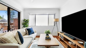 A modern living room with a sofa, coffee table, and TV stand. - Coastal 2-bed With Balcony, 200m From Beach (Gold Coast)