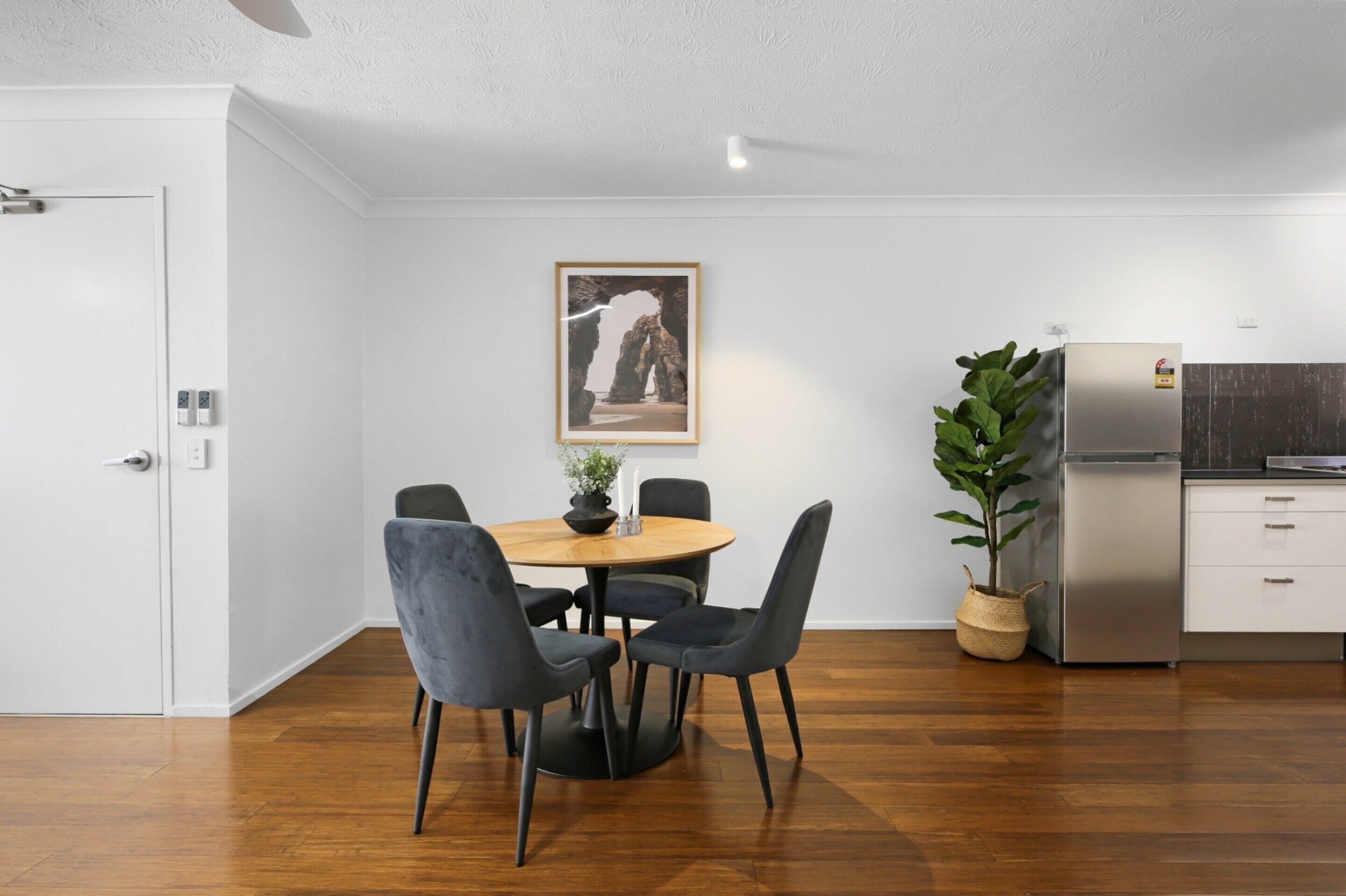 Une cuisine moderne dotée d’un réfrigérateur encastré, un coin repas avec une table ronde et des chaises, et un tableau encadré accroché au mur.