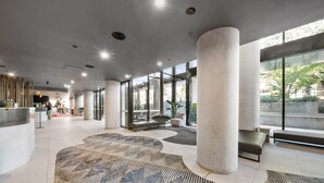 A spacious lobby with large columns, a patterned carpet, and a seating area with a view of greenery outside. - Central 1-bed Apartment With Pool (Canberra)