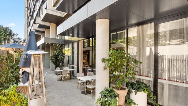 An outdoor seating area with tables and chairs, potted plants, and a grill. - Central 1-bed Apartment With Pool (Canberra)