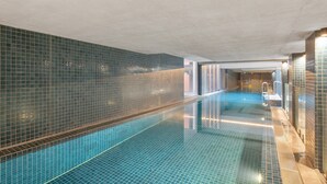 A swimming pool with tiled walls and a clear blue floor, a changing room with a bench, and a door leading to another area. - Central 1-bed Apartment With Pool (Canberra)
