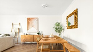 Een eethoek met een houten tafel, stoelen en een bankje. Achtergrond bevat een witte bank en een houten kast.
