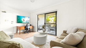 Een moderne woonkamer met een bank, een salontafel, een bureau met stoel en een groot raam met uitzicht op groen.
