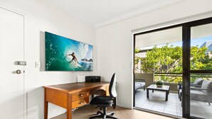 Een moderne kantoorruimte met een houten bureau, een zwarte bureaustoel en een groot schilderij van een surfer op een golf.