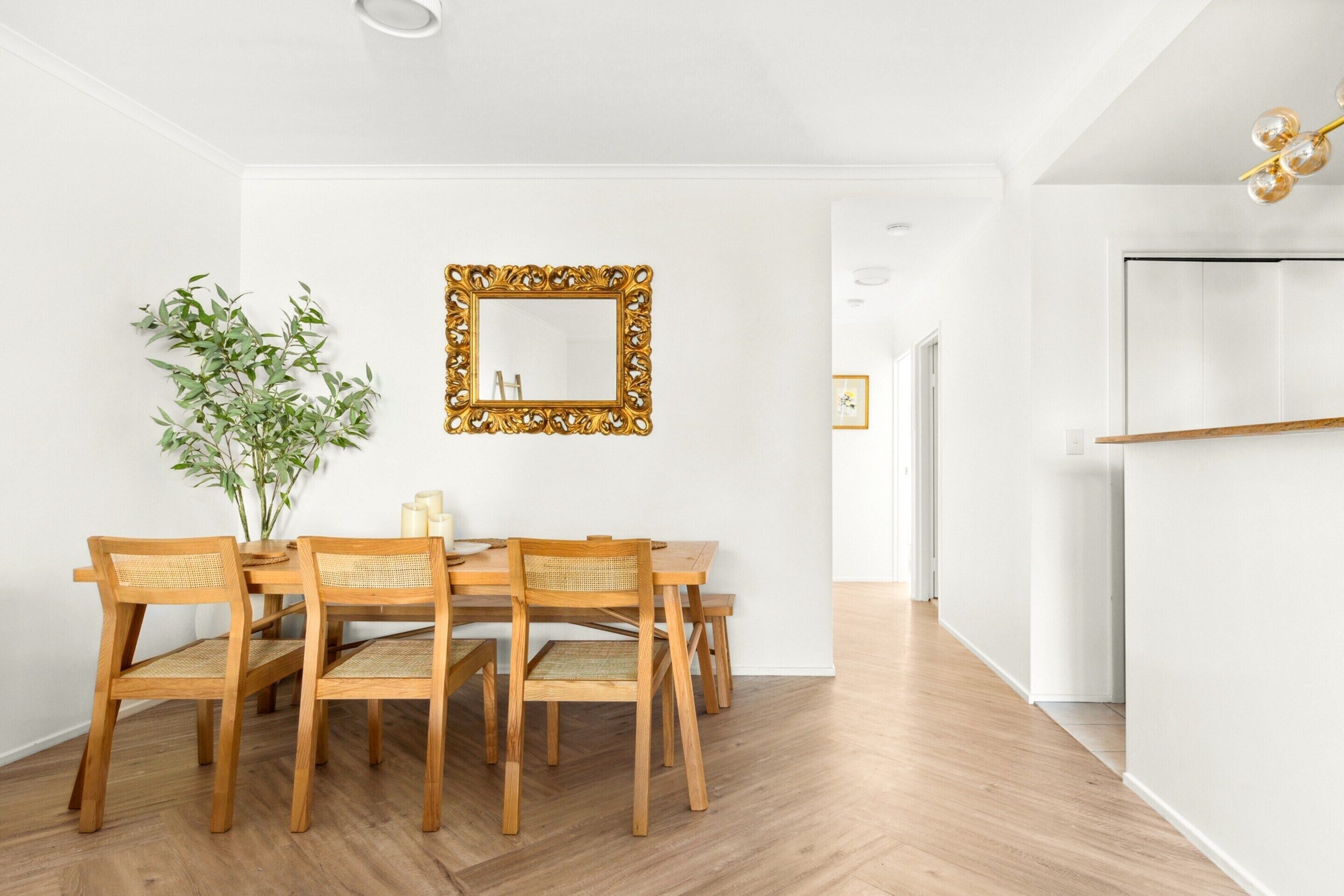 A dining area with a wooden table and chairs, a mirror with an ornate frame, and a potted plant.