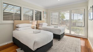 A bedroom with two beds, large windows with blinds, a ceiling light, and a view of the outside.