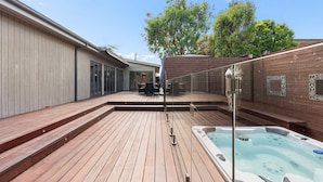 A wooden deck with a hot tub, outdoor furniture, and a view of a house in the background.