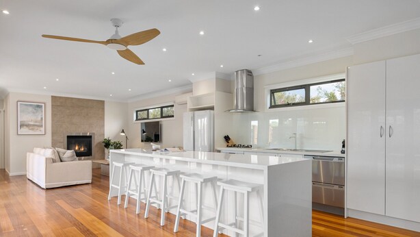 A modern kitchen with white bar stools, a central island, and stainless steel appliances.