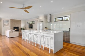A modern kitchen with white bar stools, a central island, and stainless steel appliances. - Luxurious 3-bed Home With Outdoor Spa (Melbourne)