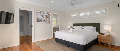 A bedroom with a bed, bedside lamps, a ceiling fan, and a TV on the wall.
