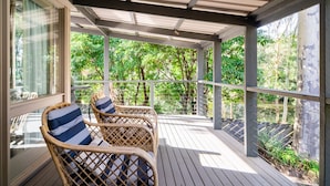 A covered outdoor deck with wicker chairs and a view of a wooded area. - Secluded 3-bed Retreat Moments to the Beach (Surf Beach)