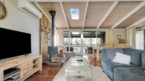 A spacious living room with a large flat-screen TV, wooden furniture, a cozy fireplace, and a view of the outdoors. - Secluded 3-bed Retreat Moments to the Beach (Surf Beach)
