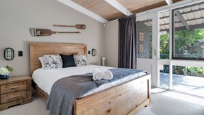 A bedroom with a wooden bed, a nightstand, a wall-mounted lamp, and a view through a glass door. - Secluded 3-bed Retreat Moments to the Beach (Surf Beach)
