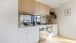A modern kitchen with white cabinetry, stainless steel appliances, and a wooden countertop. - Cosy 1-bed With Private Balcony By Showgrounds (Melbourne)