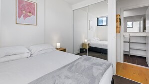 A modern bedroom with a bed, bedside tables, a mirror, and a wardrobe. - Cosy 1-bed With Private Balcony By Showgrounds (Melbourne)