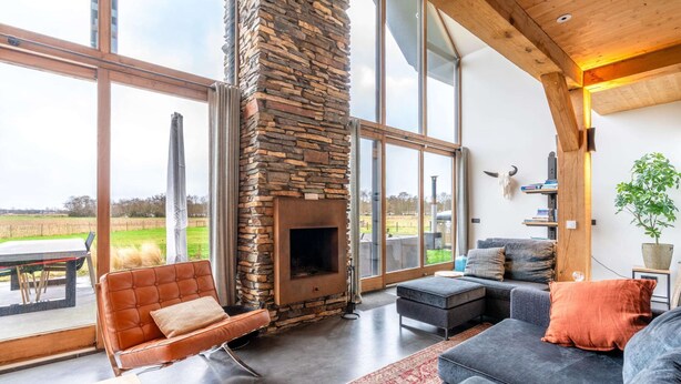 A modern living room with a stone fireplace, large windows, and a view of the outdoors.