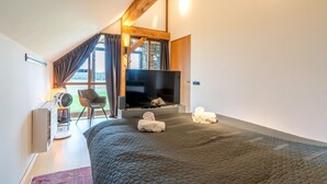 A modern bedroom with a large bed, a flat-screen TV, a fan, and a view of the outdoors.