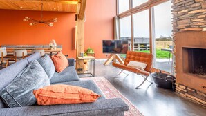 A modern living room with a stone fireplace, a large window, and a dining area with a wooden ceiling.
