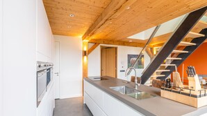 A modern kitchen with a wooden ceiling, a large island with a sink, and a staircase leading to another level.