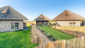 A row of thatched-roof cottages with stone walls, a grassy pathway, and a wooden fence.