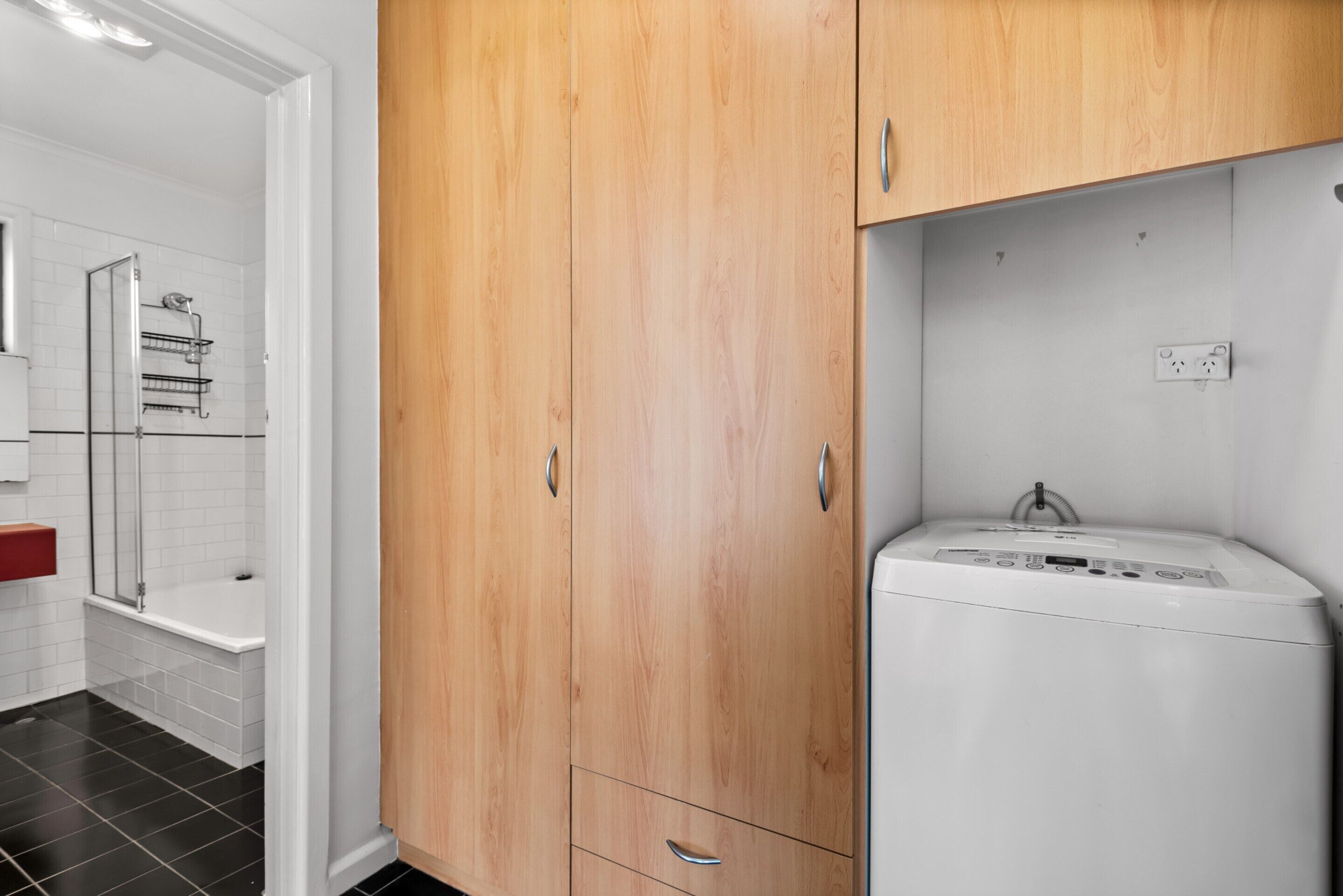 A bathroom with a wooden cabinet, a white washing machine, and a shower area.