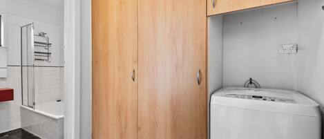 A bathroom with a wooden cabinet, a white washing machine, and a shower area.