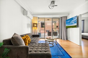 Ein modernes Wohnzimmer mit einer Couch, einem kleinen runden Tisch und einem großen Fenster mit Blick auf ein Gebäude.