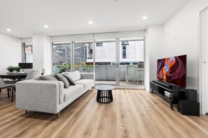 A modern living room with a grey sofa, a round coffee table, and a flat-screen TV. - Sleek South Yarra 2-bed With Alfresco Dining (Melbourne)