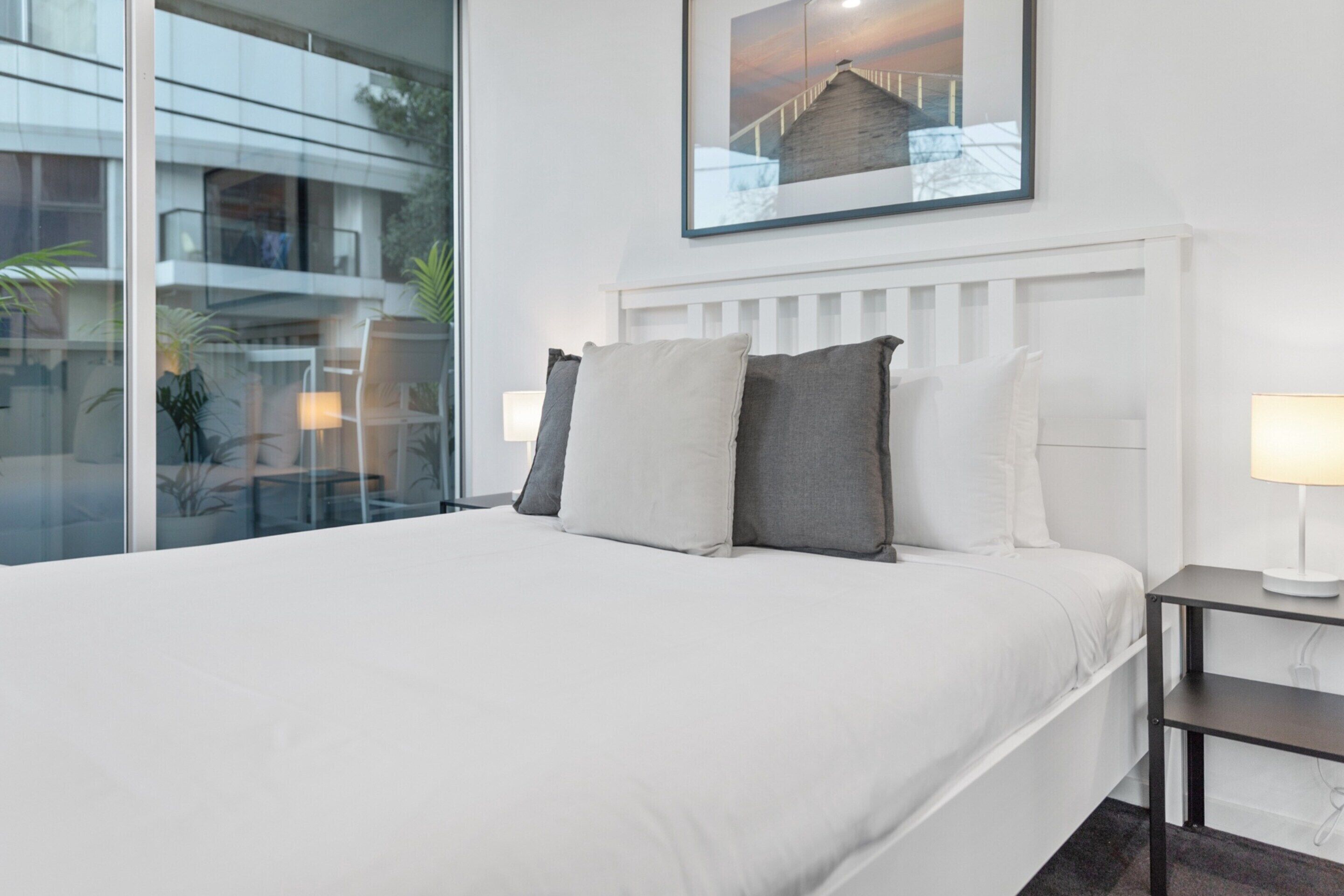 Una habitación de hotel con una cama grande, una mesita de noche con lámpara, una ventana con vistas al exterior y un cuadro enmarcado en la pared.