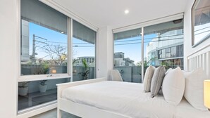 Camera da letto moderna con un letto grande, pareti bianche e ampie finestre che offrono vista sulla città.