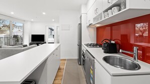 Una cucina moderna con mobili bianchi, lavello in acciaio inossidabile e una parete d'accento rossa.