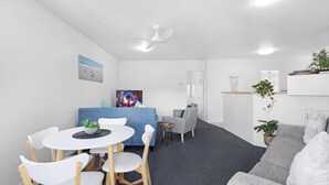 Un salon moderne avec un canapé bleu, un fauteuil gris, une table à manger blanche avec des chaises et un ventilateur de plafond.