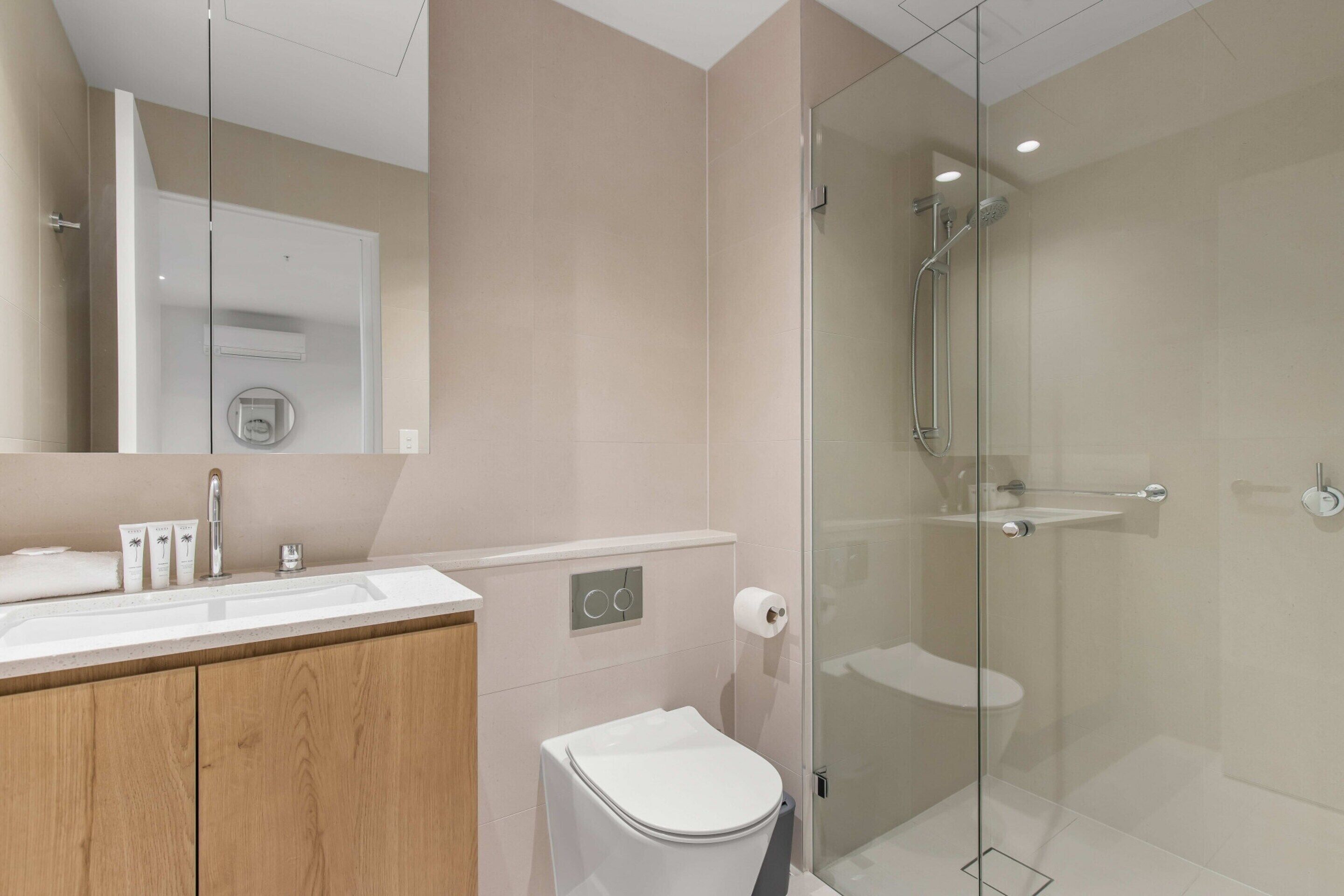 Ein modernes Badezimmer mit einer Duschkabine aus Glas, einem Holzbadezimmer-Möbel und einer Toilette.