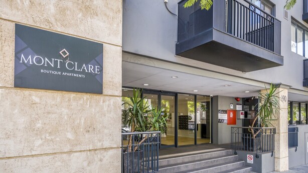 L’entrée d’un immeuble, avec une enseigne indiquant : « MONT CLARE – APPARTEMENTS DE LUXE ».