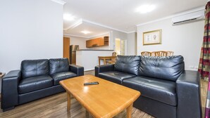 Un salon avec deux canapés en cuir noir, une table basse en bois et un coin repas comprenant une table et des chaises.