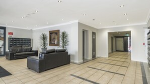 Un hall d’entrée spacieux, avec un canapé en cuir noir, une plante en pot et un tableau encadré au mur.