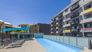 Une piscine sur le toit, dotée de chaises longues et surmontée d’un auvent bleu.