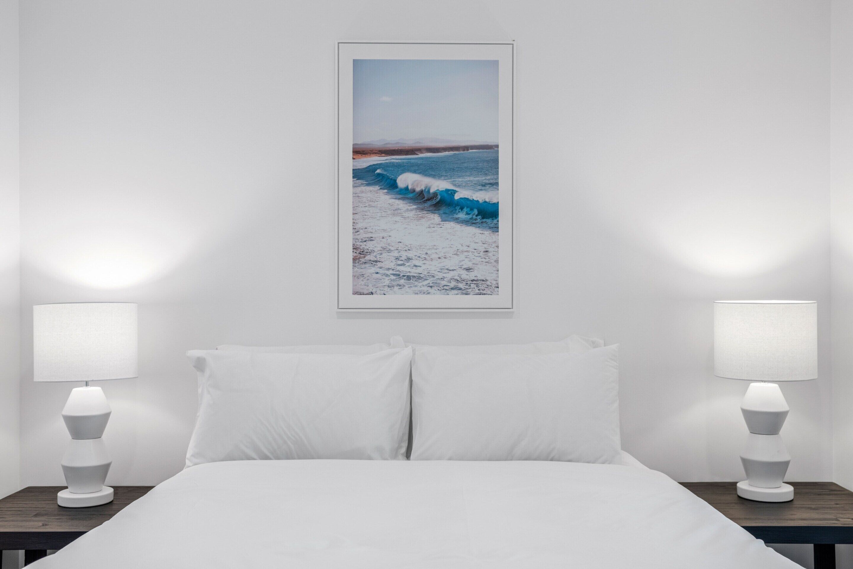 Een hotelkamer met een bed, twee bedlampjes en een ingelijst strandlandschap aan de muur.
