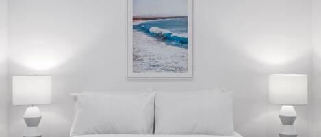 Habitación de hotel con cama, dos lámparas de noche y un cuadro con una escena de playa en la pared.