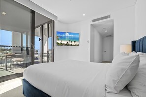 Ein Hotelzimmer mit einem großen Bett, einem Balkon mit Glastür sowie einem Wand-Fernseher und Blick auf den Strand.