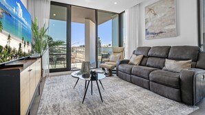 A modern living room with a leather sofa, a glass coffee table, and a large painting of a beach scene. - Stylish 2-bed Apartment With Rooftop BBQ Access (Perth)