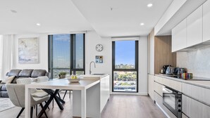 A modern kitchen with white cabinets, a large window, and a dining area with a white table and chairs. - Stylish 2-bed Apartment With Rooftop BBQ Access (Perth)