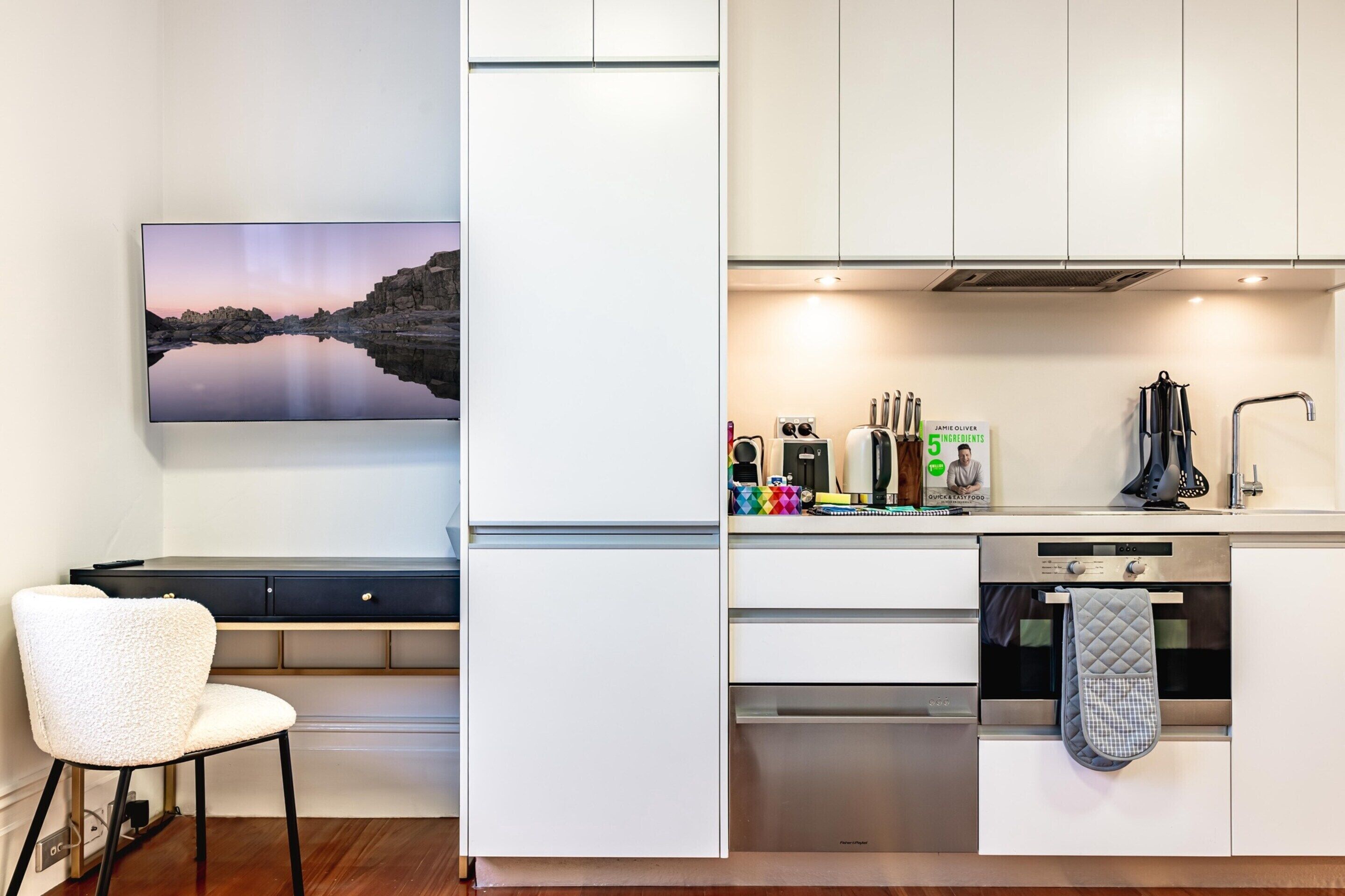 A modern kitchen with white cabinetry, a built-in oven, and a countertop with various appliances.