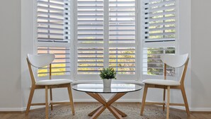 A room with a round glass table, two white chairs, and a potted plant. - Elegant 3-bed Home From Sunny Glenelg Beach (Adelaide)
