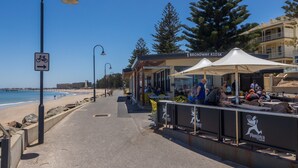 A coastal walkway with a bike path sign, a kiosk named 'Broadway Kiosk', and outdoor seating with people. - Elegant 3-bed Home From Sunny Glenelg Beach (Adelaide)
