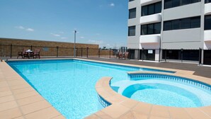 Una piscina de diseño curvo, rodeada por una valla y un edificio con amplias ventanas.